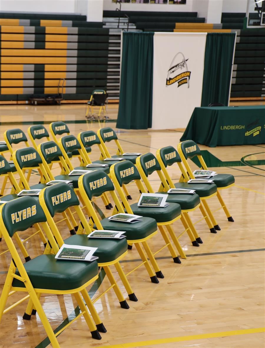  Empty chairs set up with signing day programs, and table in background.